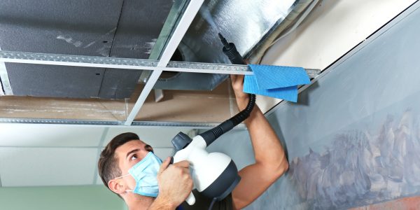 Male technician cleaning industrial air conditioner indoors